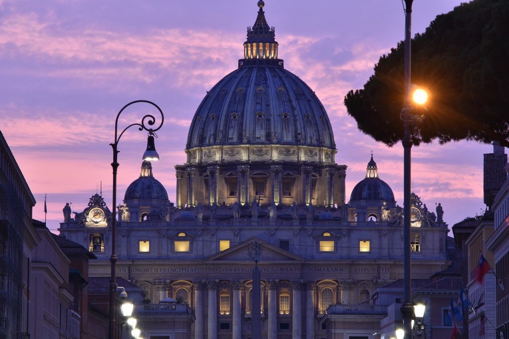 St. Peter's Basilica at sunset during Jubilee 2025 in Rome, illuminated dome and Vatican City skyline with pink and purple sky.