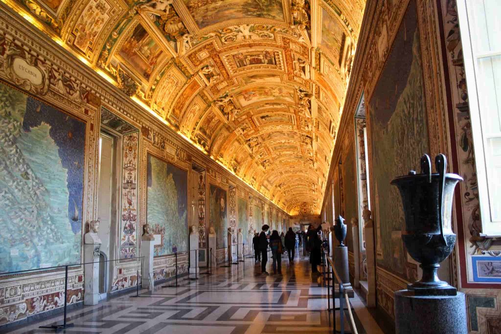 Interior of the Gallery of Maps in the Vatican Museums, featuring a frescoed ceiling and historical maps along the walls, lit by natural light.