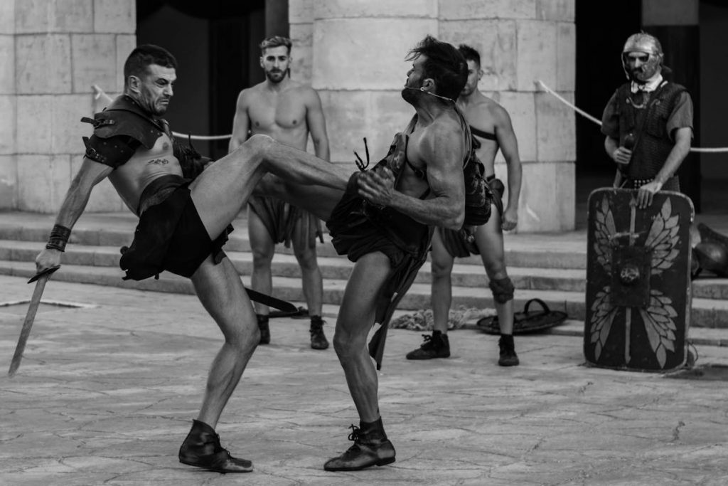 Reenactment of gladiator fight in ancient Roman costume at the Colosseum, showcasing combat techniques and historical armor.