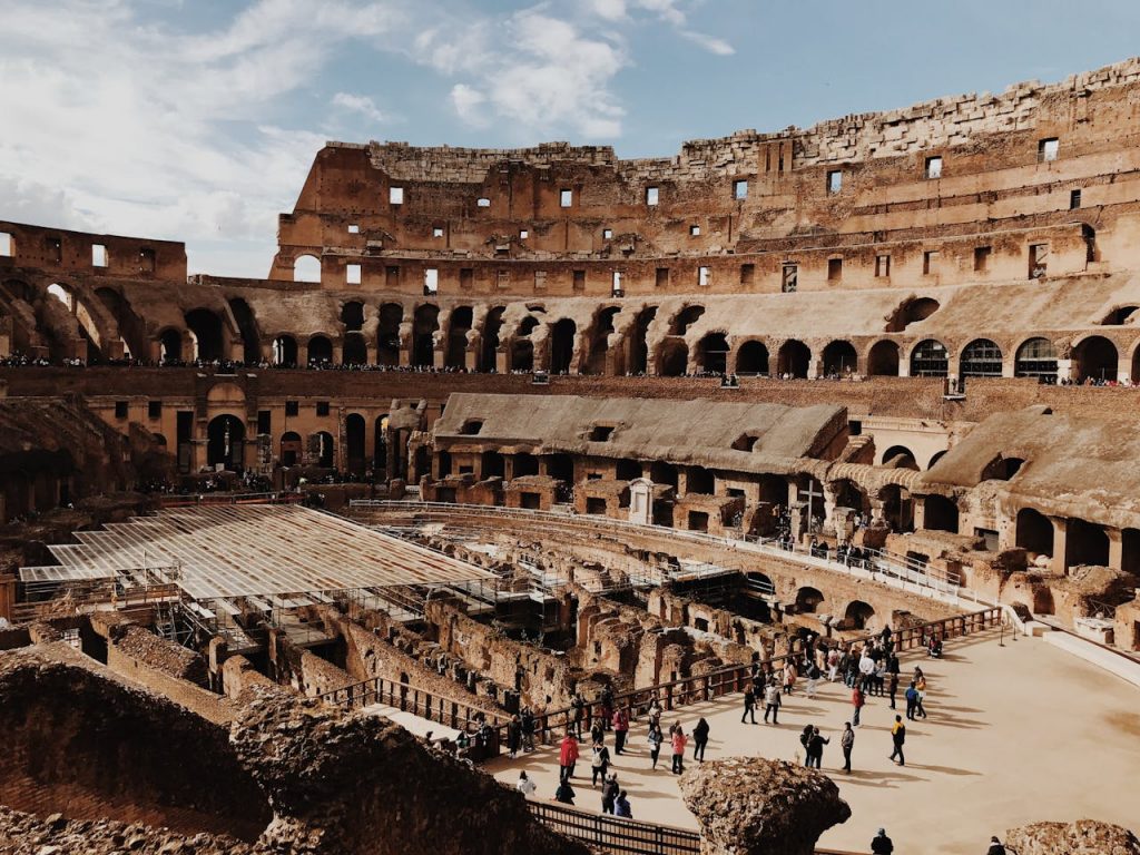 Interior view of the Colosseum in Rome with tourists exploring the ancient amphitheater and its underground structures.