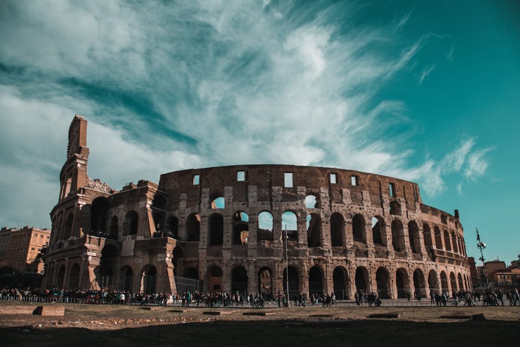 Panoramic view of the Colosseum in Rome with tourists and dramatic sky, symbol of ancient Roman architecture and history.