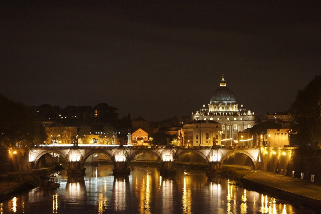 View of St. Peter's Basilica and Ponte Sant'Angelo illuminated at night, reflected in the Tiber River in Rome by night.